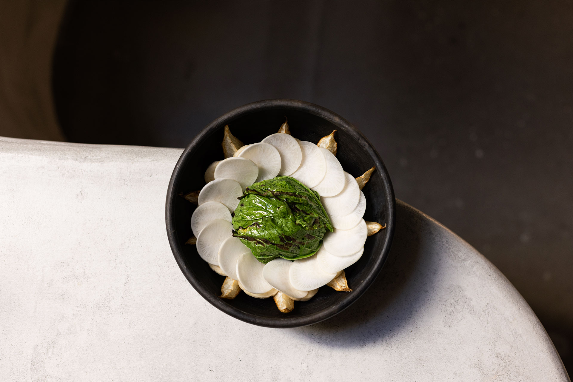 small black bowl containing grilled greens atop a circle of radishes with crab meat inside