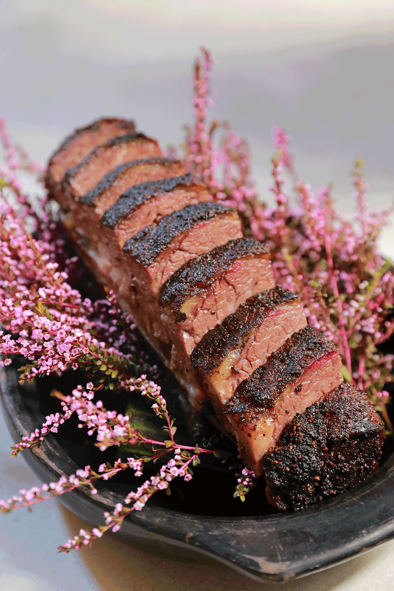 a platter with evenly-sliced medium rare stake atop of a bed of pink flowers